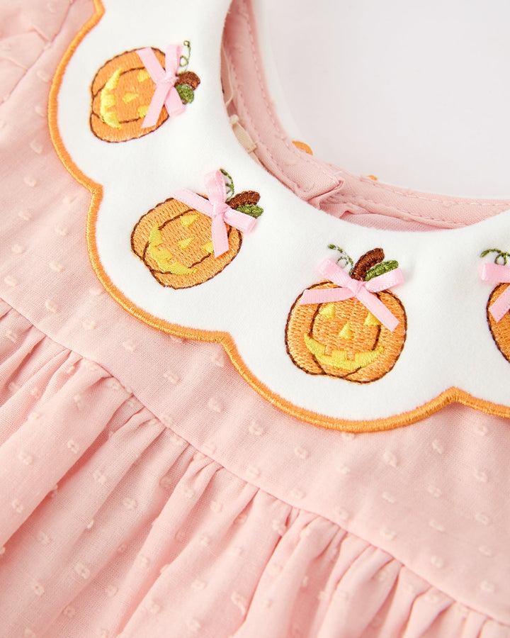 Close-up of pink dress with stitched pumpkin appliques and orange embroidered trim