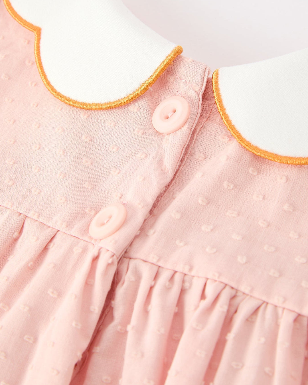 Close-up of pink button-front dress with orange scalloped collar edge