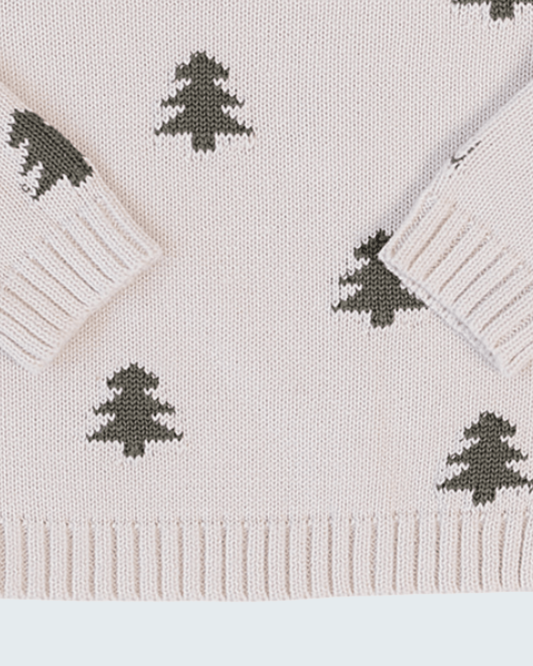 Close-up of a knit sweater in a very light blush pink with dark olive green Christmas tree motifs and ribbed cuffs, hem, and collar.