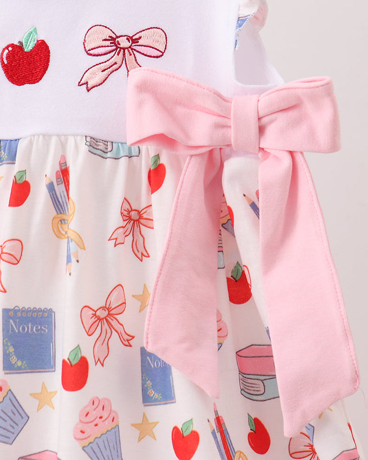Dress with a pink bow and a pattern of red apples, blue books, and colorful bows on a white background.