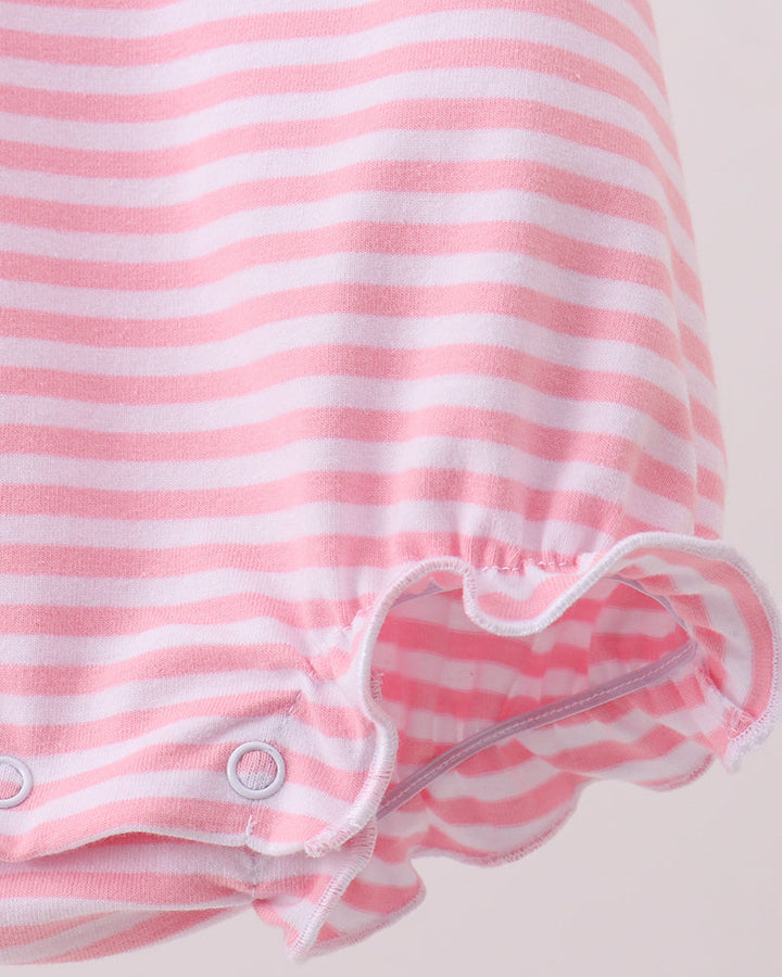 Close-up of a pink and white striped baby garment, showing the ruffled leg opening with snap closures on a light beige background.