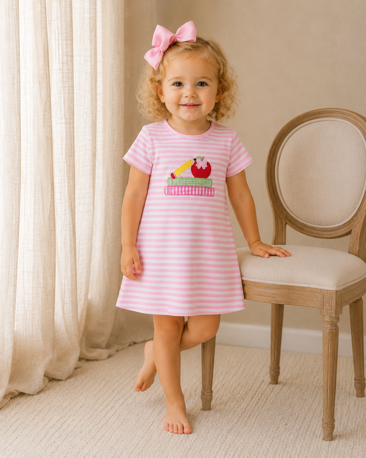 Young girl is standing by a wooden/cloth chair. 