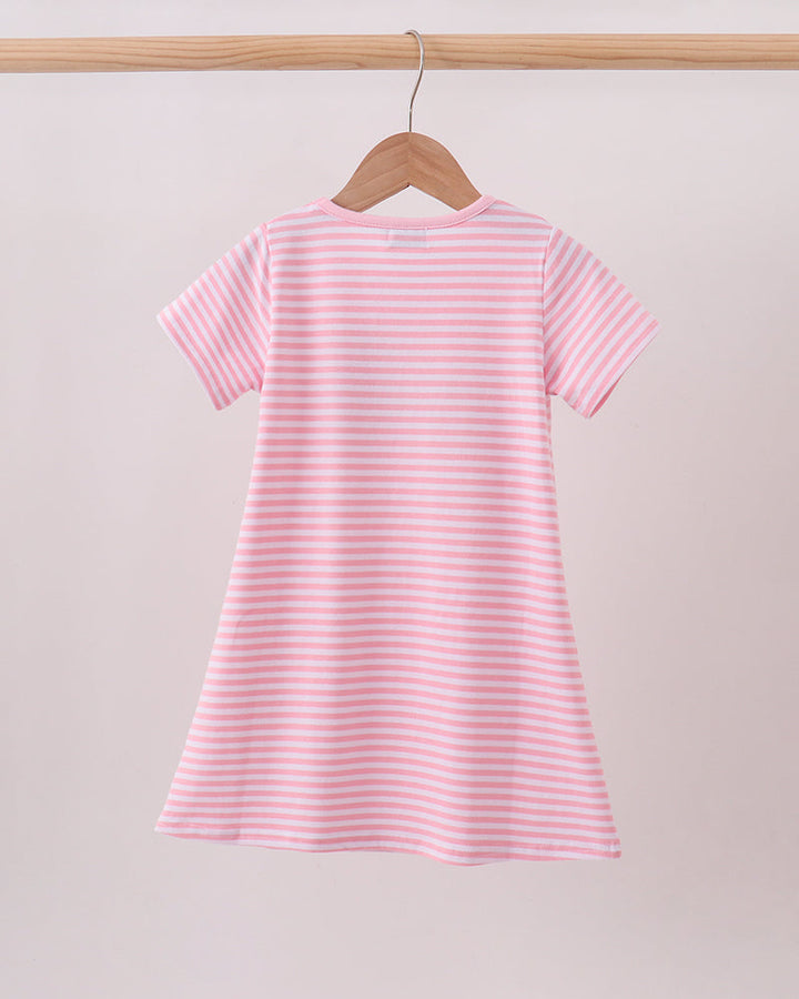 A pink and white horizontally striped short-sleeve baby dress hanging on a wooden hanger from a light wood clothing rack against a solid pale pink background.