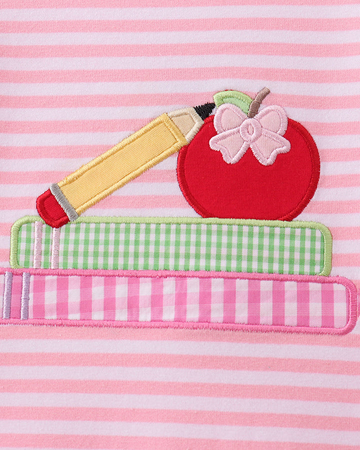 Close-up of a pink and white striped garment featuring an applique design of a red apple with a pink bow, a yellow pencil, and green-and-white checkered and pink striped layers.