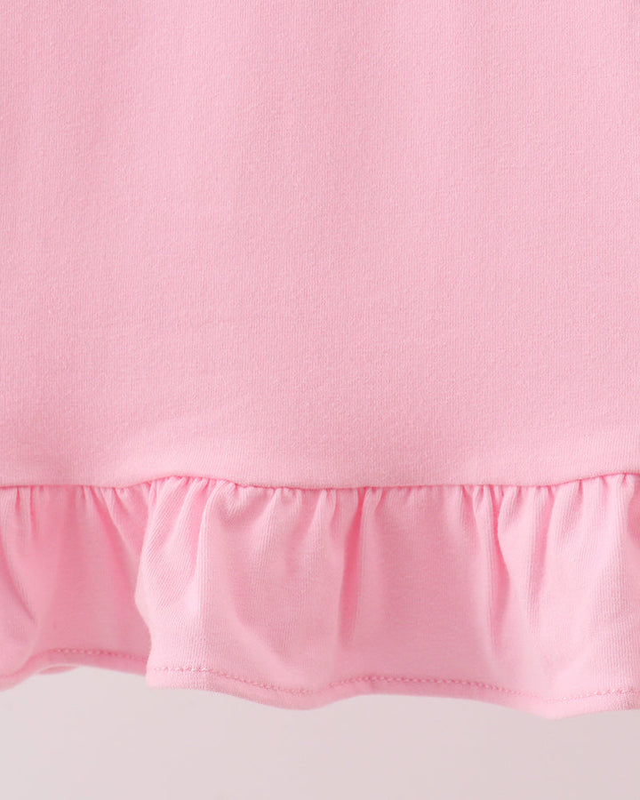 Close-up of a light pink fabric garment with a ruffled hem against a pale background.