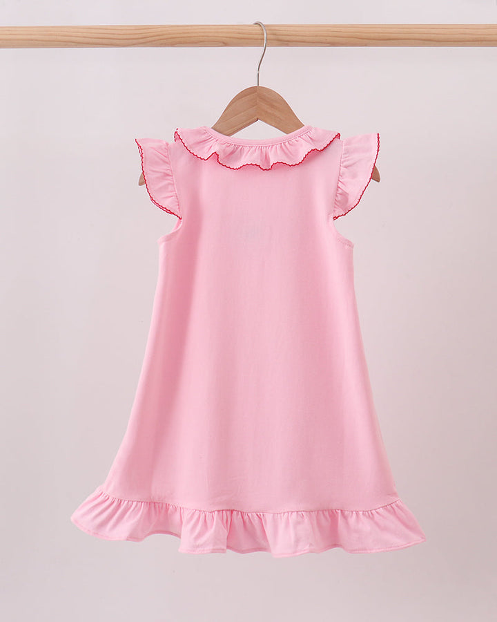 A light pink sleeveless dress with ruffled trim on the shoulders and hem, hanging on a wooden hanger from a wooden clothes rack against a plain light background.