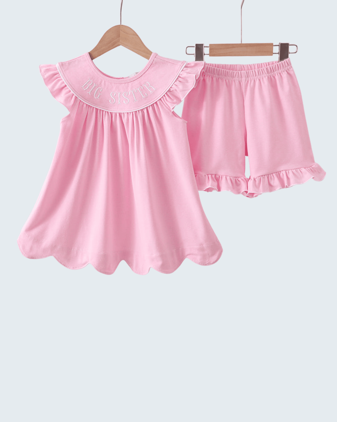 Pink children's dress and shorts set on hangers against a white background