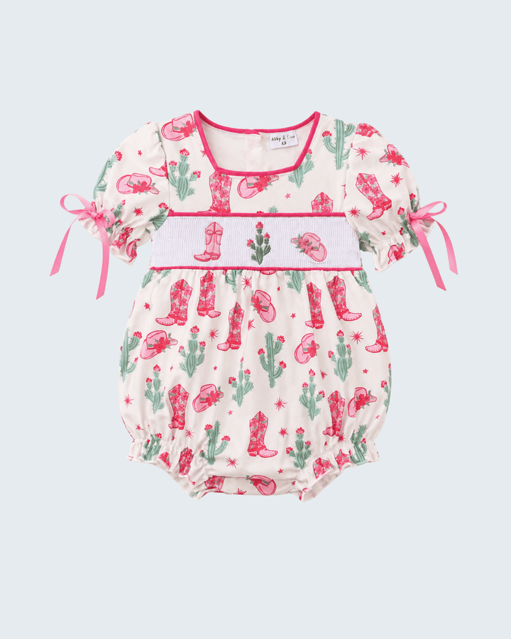 Baby romper with cactus and cowboy boot pattern on a light blue background