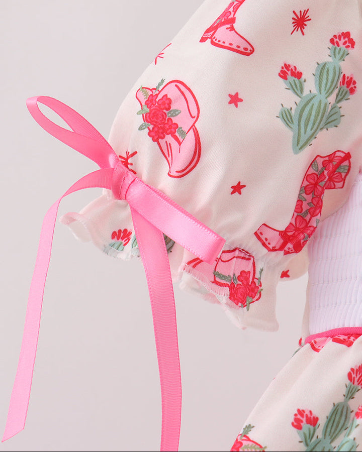 Baby outfit with cactus and boot pattern and pink ribbon on a light gray background