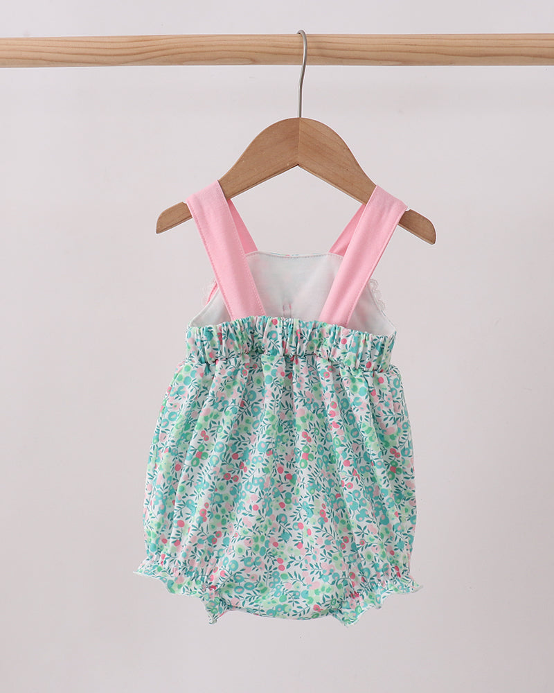Floral baby romper with pink straps on a wooden hanger against a white background