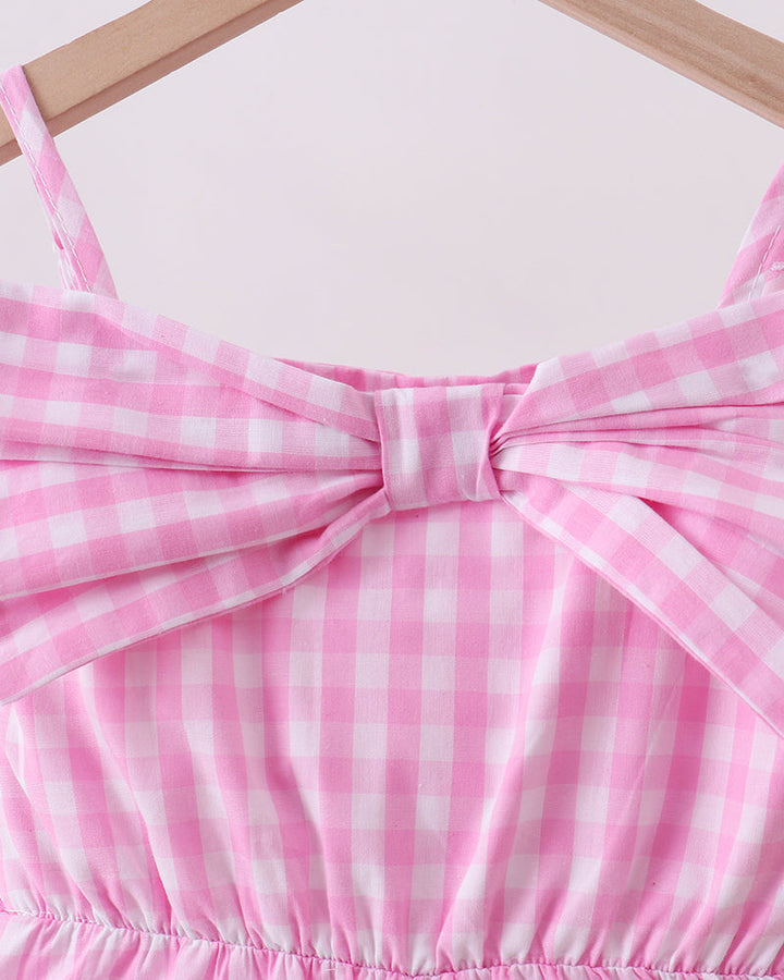 Close-up of a pink and white checkered dress with a bow detail on a light background.