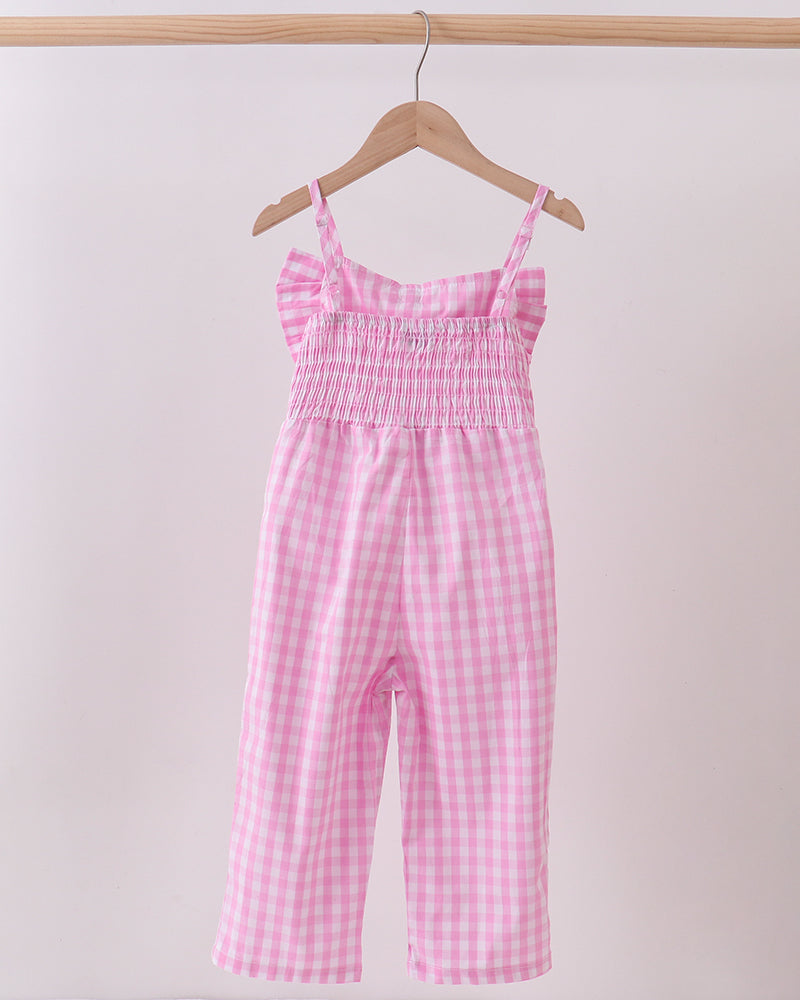 Pink checkered jumpsuit hanging on a wooden hanger against a light pink background