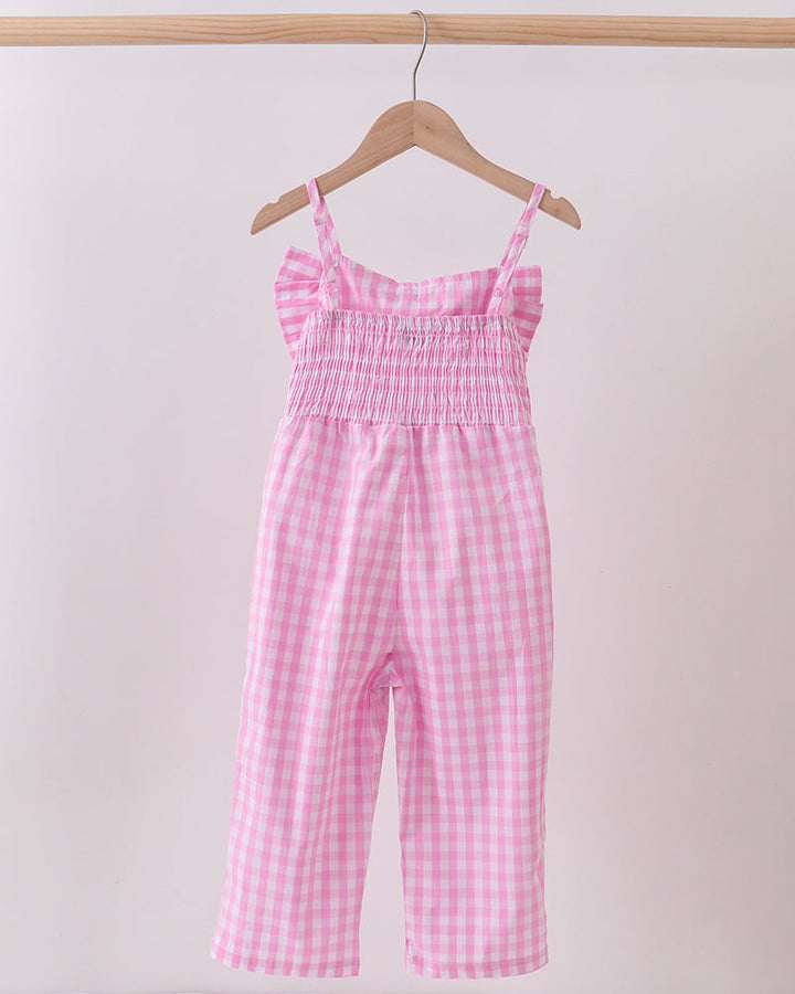 Pink checkered jumpsuit hanging on a wooden hanger against a light pink background