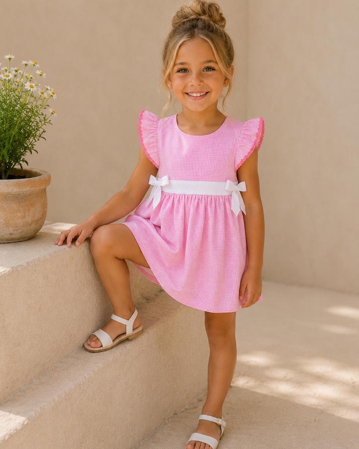 Young girl in a pink dress with white sandals sitting on a stone ledge.