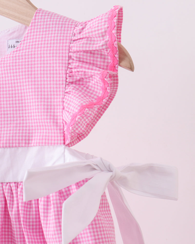 Pink gingham dress with white ribbon on a light pink background