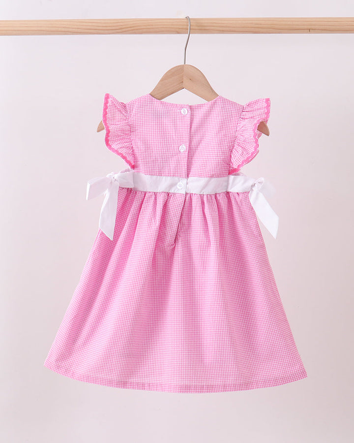 Pink checkered dress with white ribbon belt on a wooden hanger against a light pink background