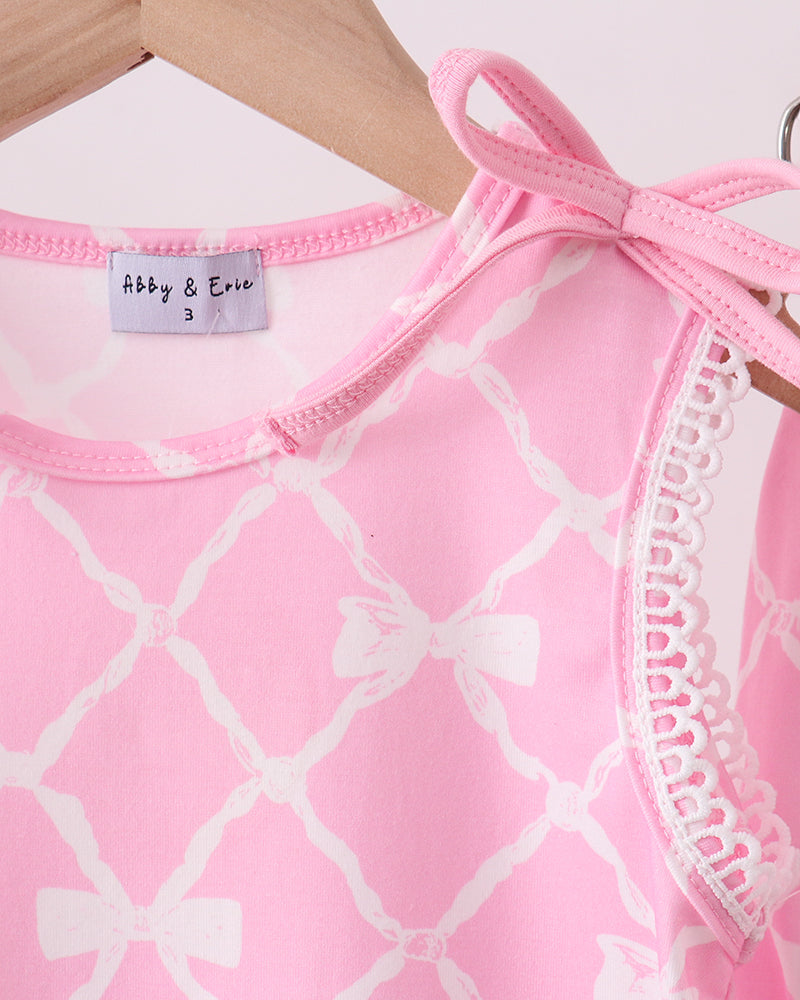 Pink and white patterned baby outfit with lace trim on a wooden surface