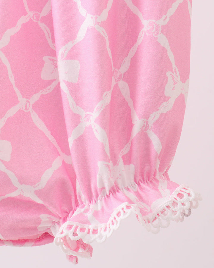 Pink baby bloomers with white lattice pattern and ruffled edge on a light pink background