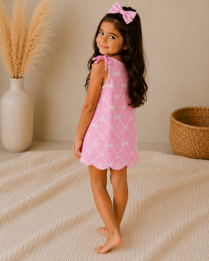 Young girl in a pink dress with white patterns standing in a room with a neutral background.