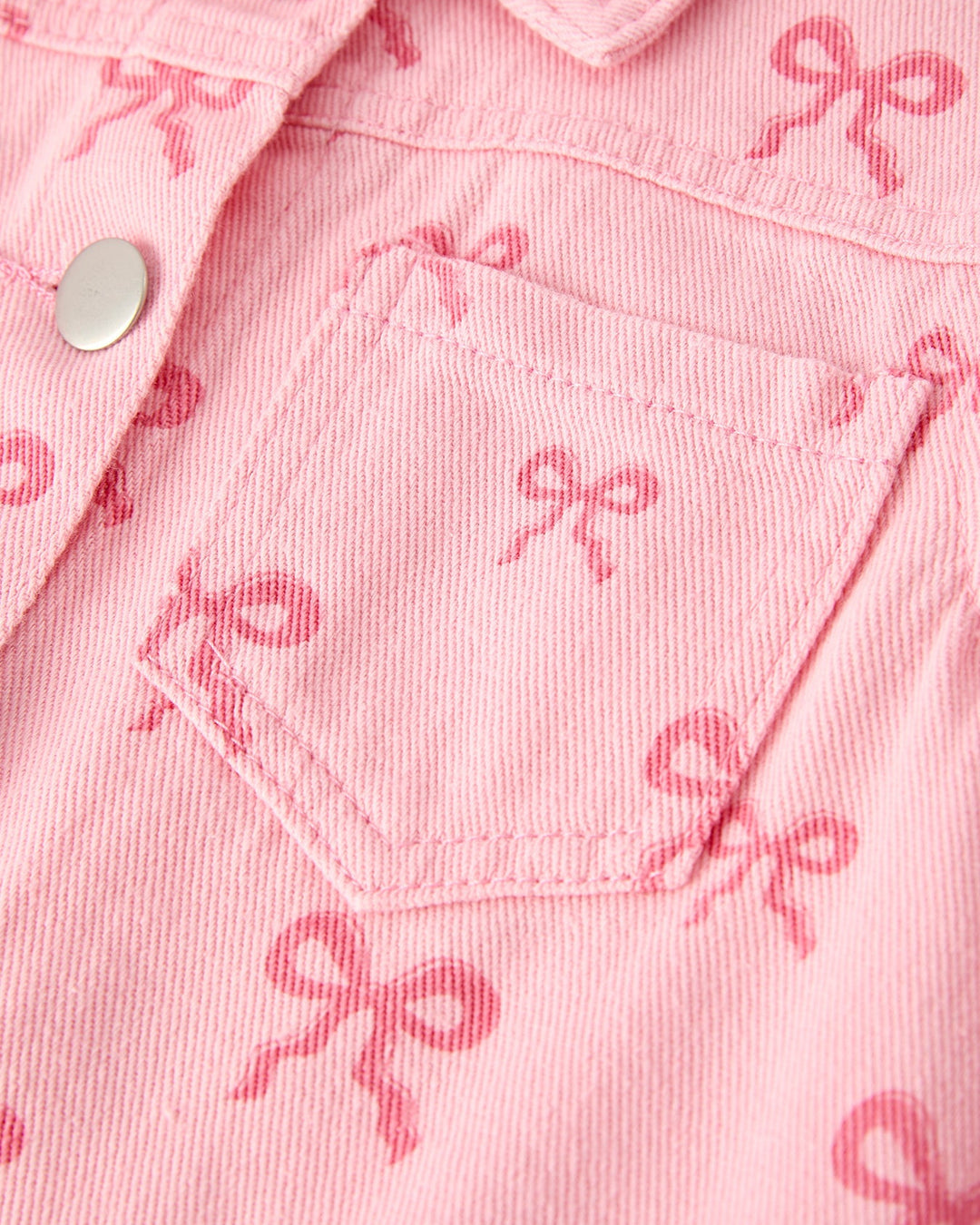 Pink denim jacket close-up: bow print fabric and stitched chest pocket
