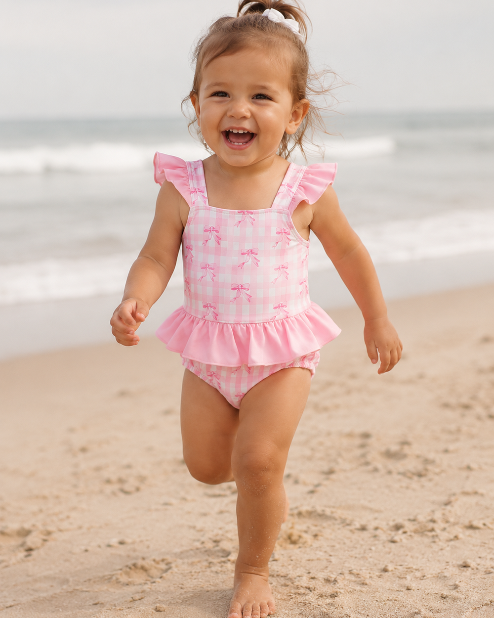 Baby girl running on beach in Pink Bow Print Ruffle One-Piece Swimsuit