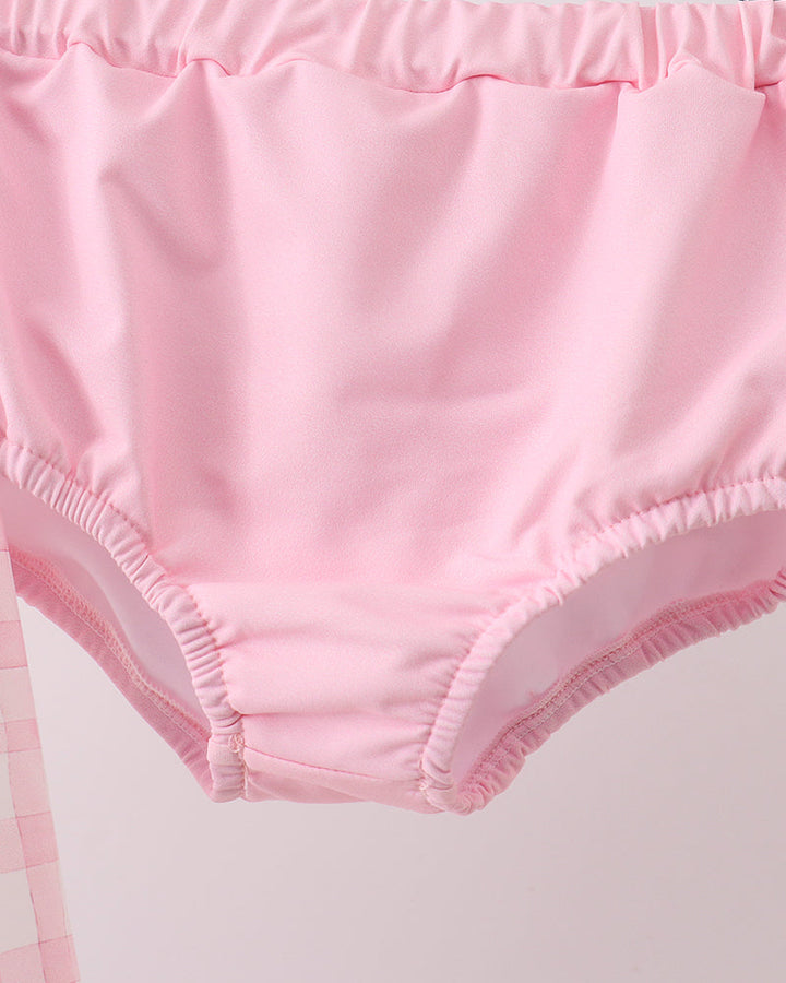 Pink swim bottoms on a wooden hanger against a white background