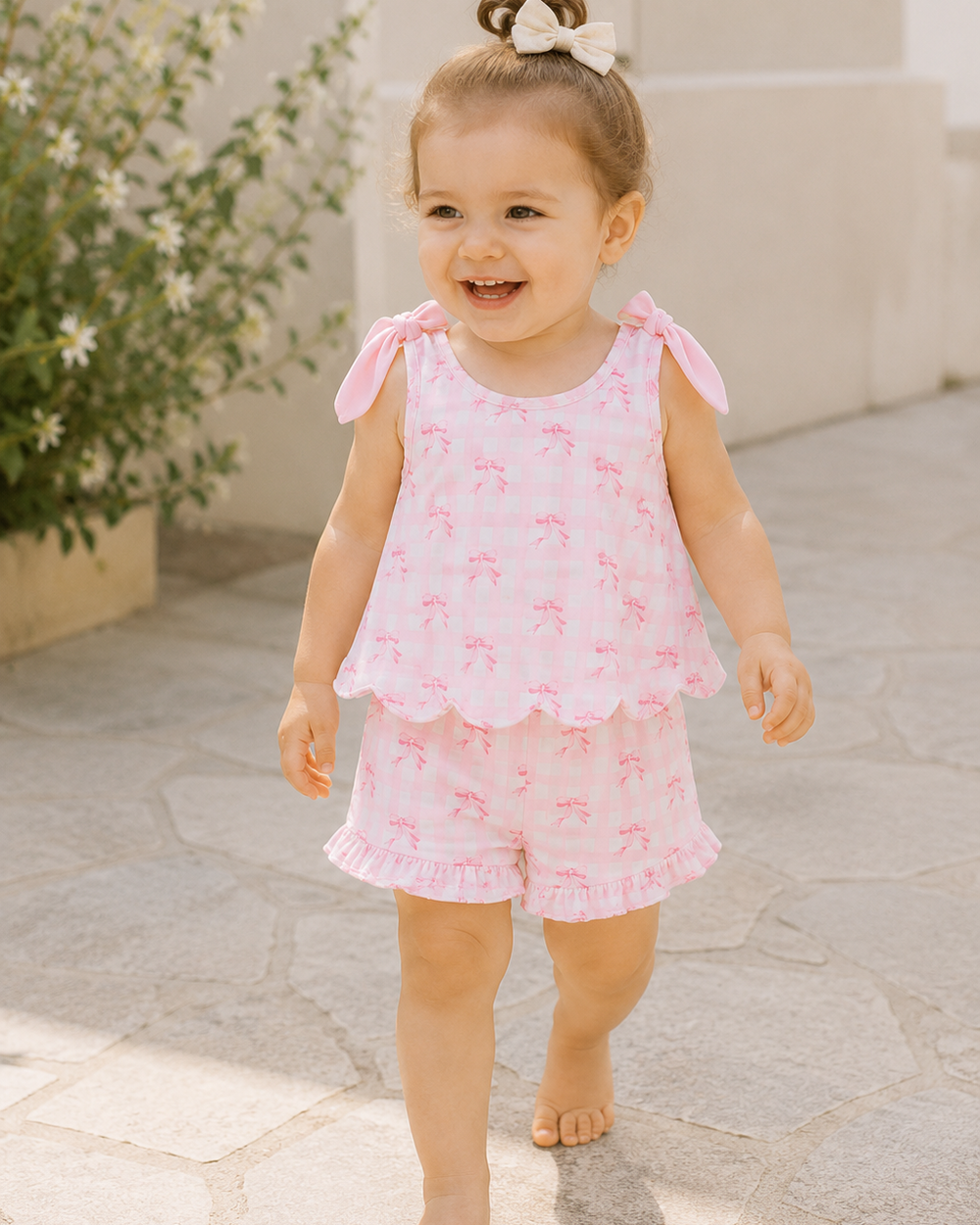 Child wearing a pink outfit with ruffled sleeves and shorts, standing on a stone path.