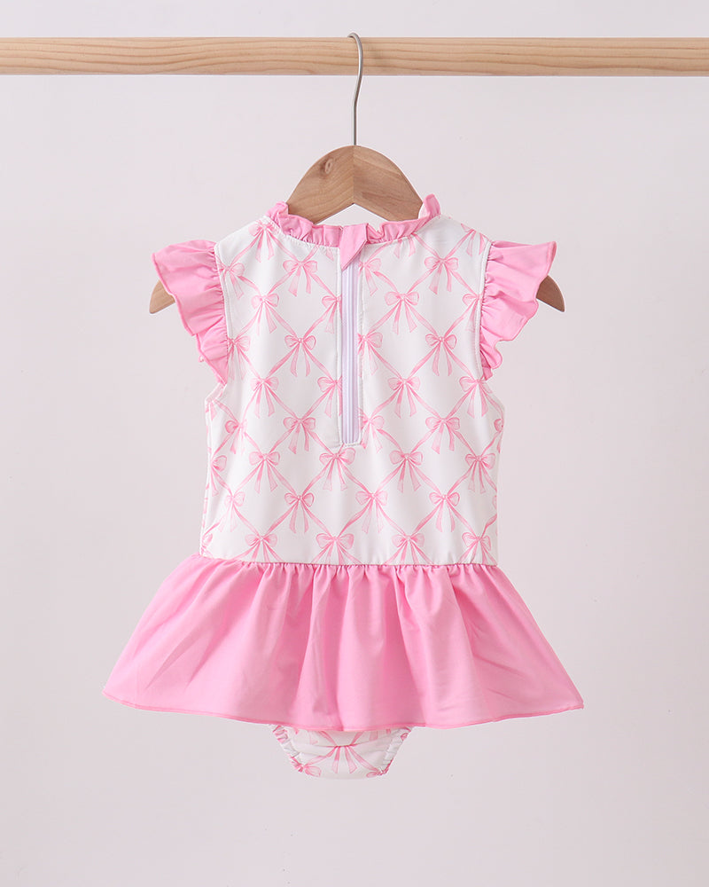 Pink and white swimsuit with ruffled details on a hanger against a light gray background