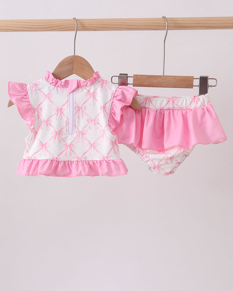 Pink and white swimsuit with top and diaper on hangers against a light gray background