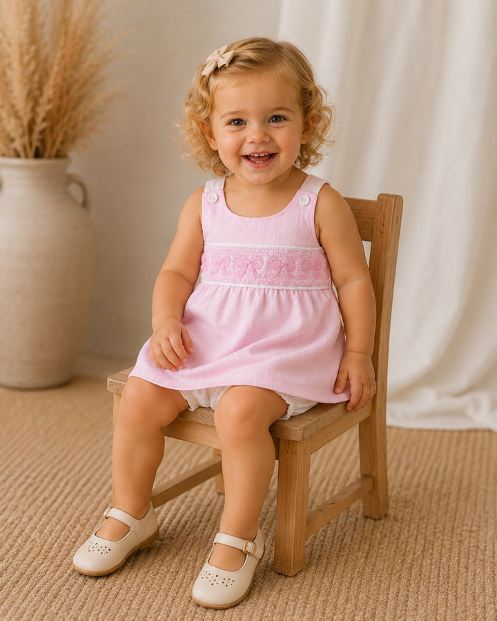 Child in a pink dress sitting on a wooden chair with a neutral background