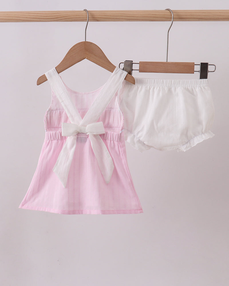 Pink dress and white shorts on hangers against a light pink background