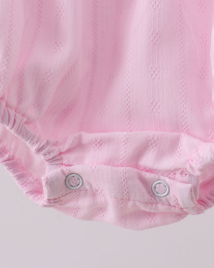 Close-up of a pink baby romper with button details on a light gray background
