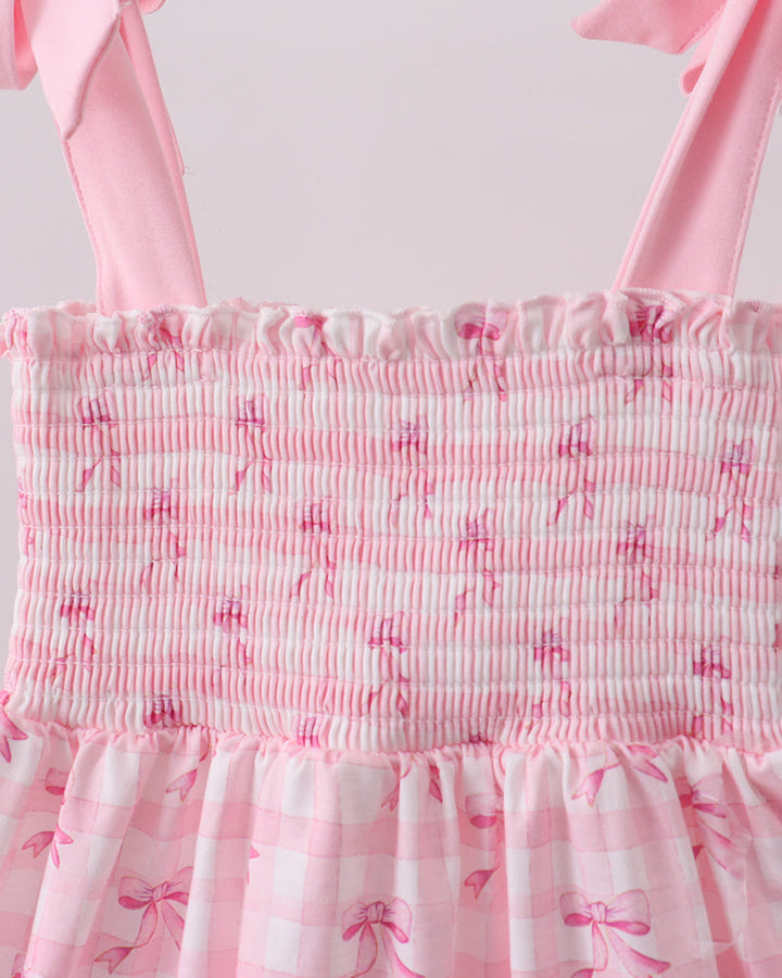 Pink dress with ruffled details and bow straps on a white background