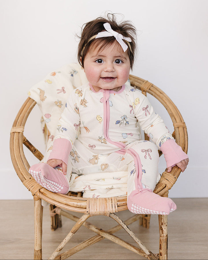 Baby sitting in a small chair wearing a white outfit with pink accents and a headband.