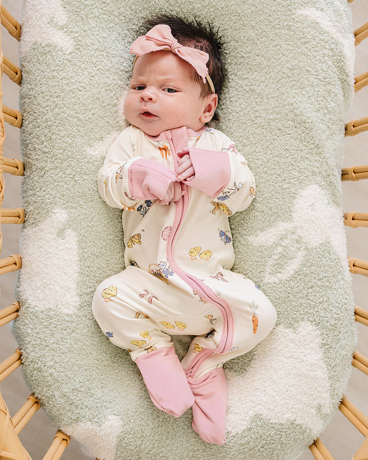 Baby in a crib with a green blanket and pink headband