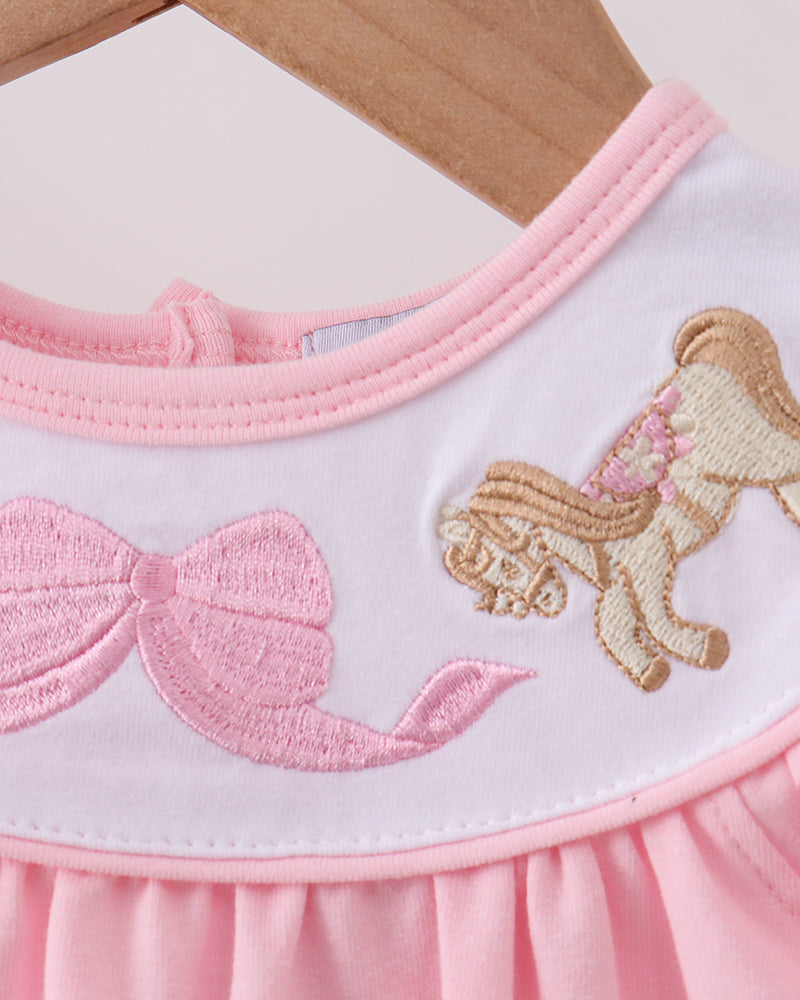 Close-up of a pink dress with a horse and bow design on a wooden surface