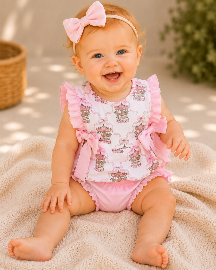 Baby wearing a pink and white outfit with a bow, sitting on a beige blanket.