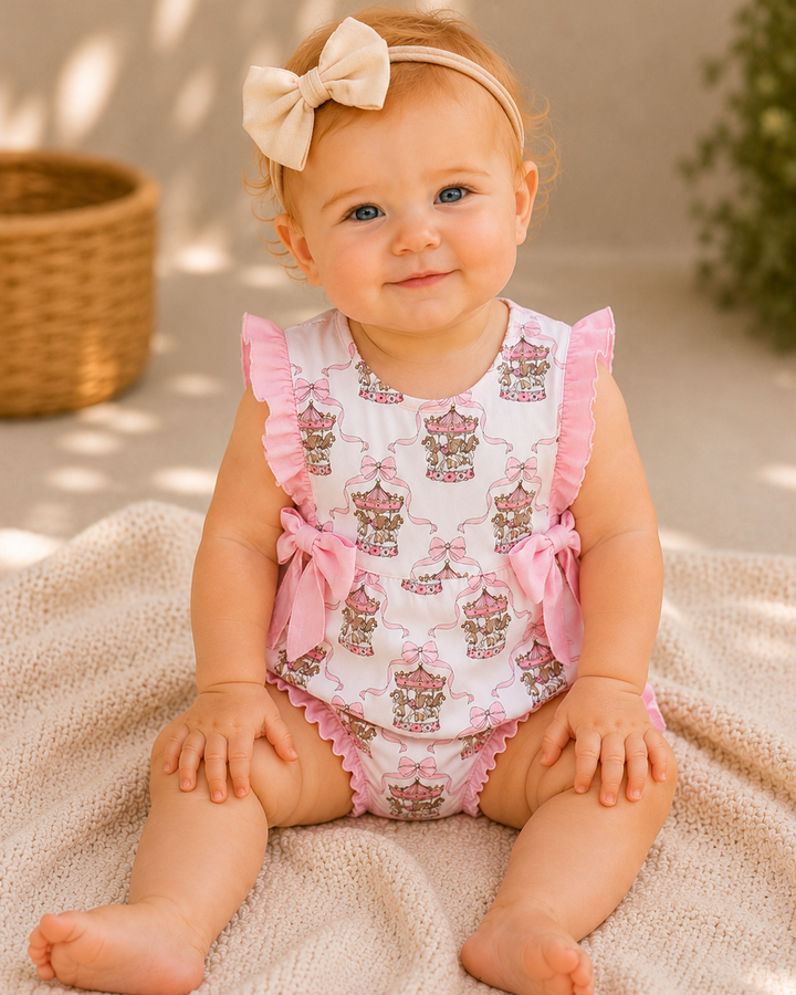 Baby wearing a pink and white romper with ruffles, sitting on a textured surface.