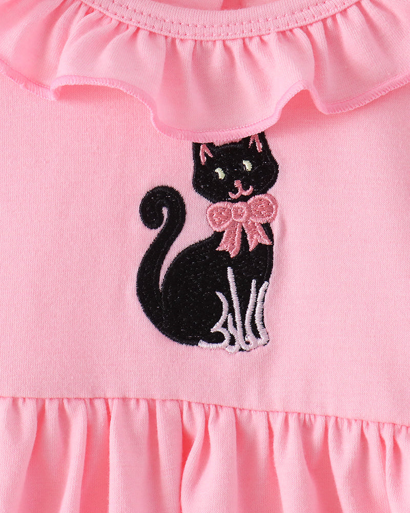 Close-up of a pink children's dress with a ruffled neckline and an embroidered black cat wearing a pink bow on the front.