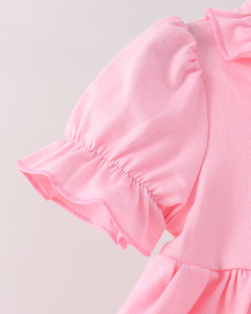 Close-up of a light pink dress featuring a ruffled short puff sleeve and a matching ruffled collar, set against a plain light gray background.