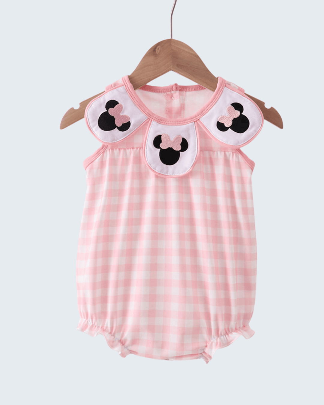 Pink checkered baby romper with cartoon character details on a hanger against a white background