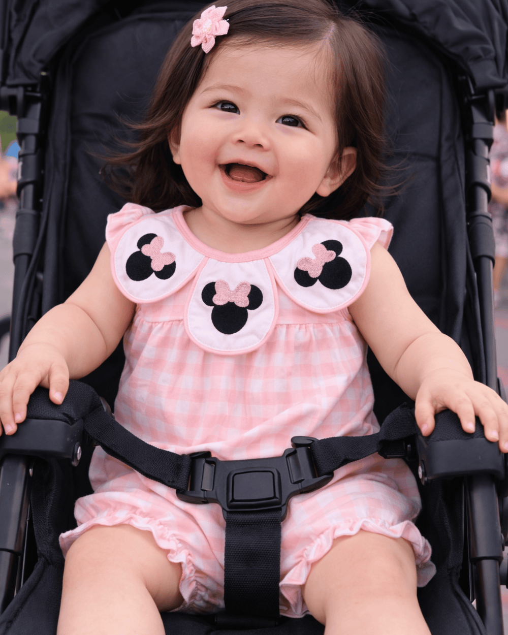 Child in a pink outfit with cartoon character design sitting in a stroller.