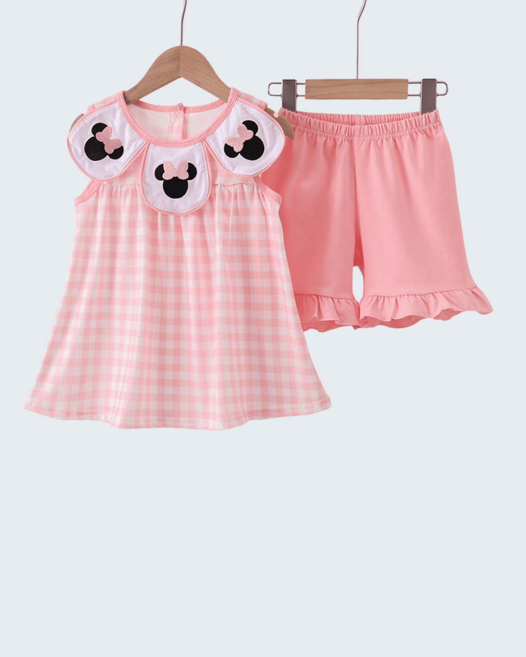 Pink checkered dress with cartoon face design and matching shorts on hangers against a white background