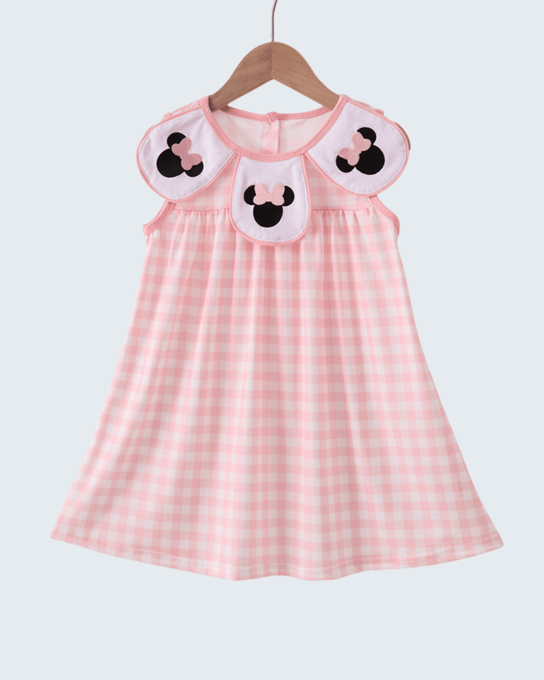 Pink checkered dress with cartoon character details on a hanger against a white background