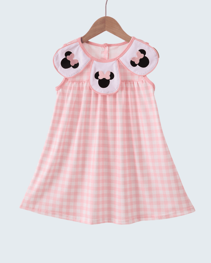 Pink checkered dress with cartoon character details on a hanger against a white background