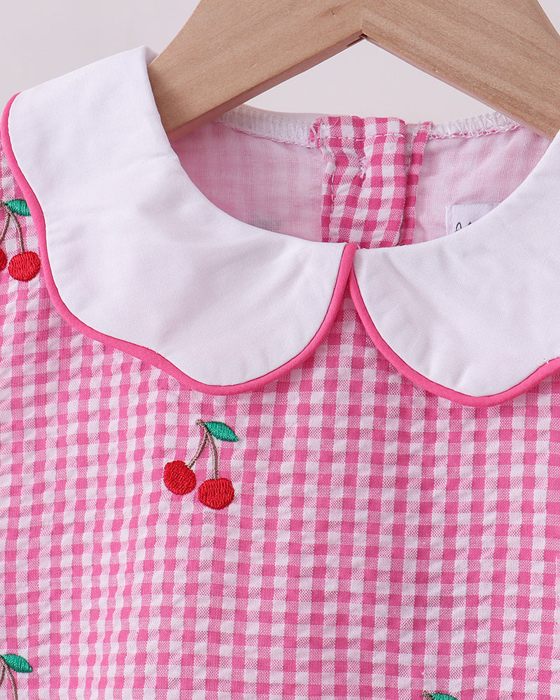 Pink gingham dress with white collar and cherry embroidery on a wooden hanger.