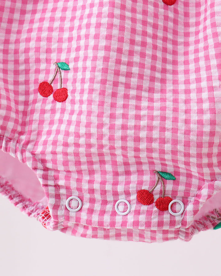 Pink gingham baby romper with cherry designs on a white background