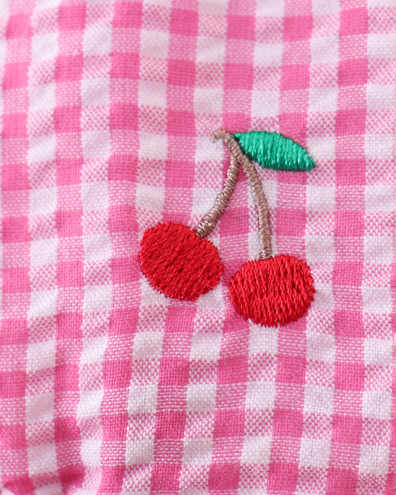 Close-up of a pink and white checkered fabric with embroidered cherries.