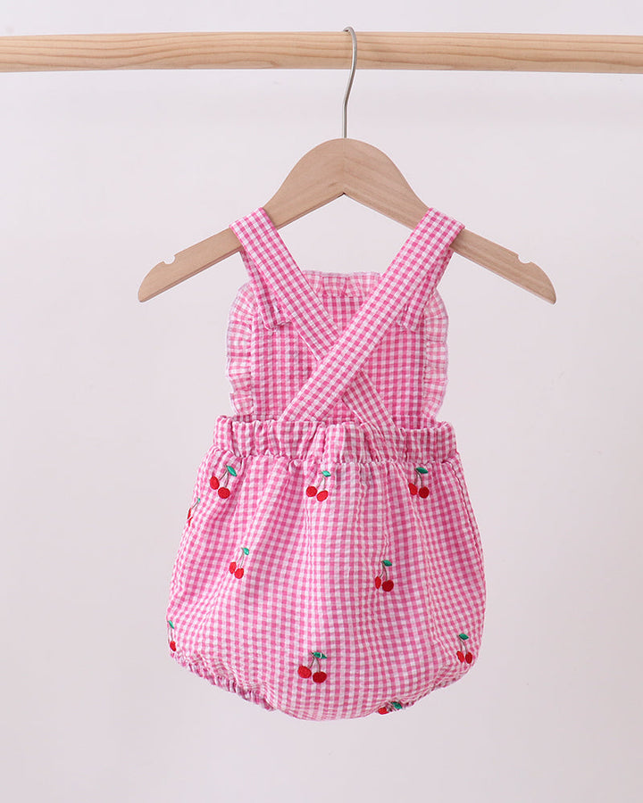 Pink gingham baby romper with cherry designs on a wooden hanger against a white background