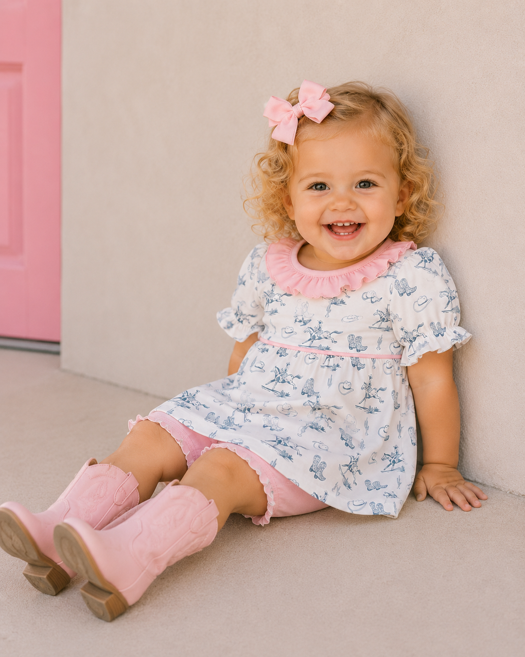 Child wearing a floral dress with pink accents and pink boots, sitting on a light-colored floor.